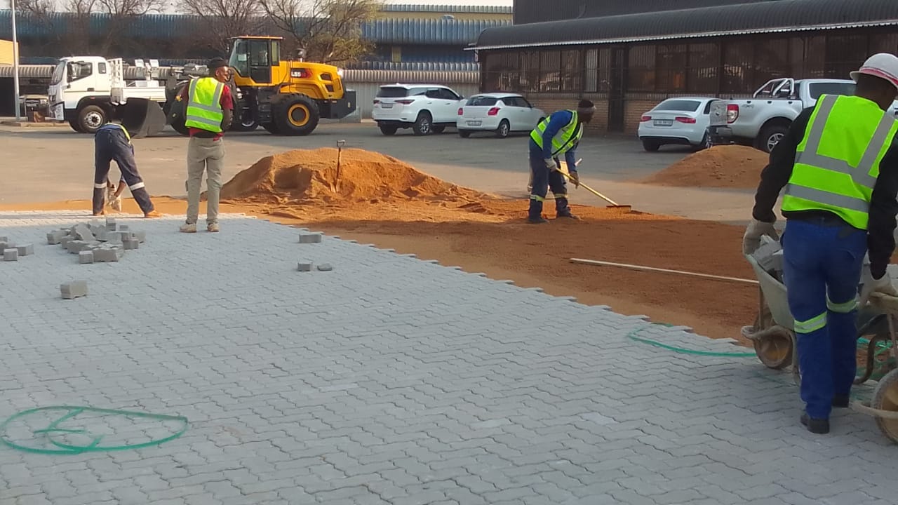 Large-scale paved area under construction with neatly laid interlocking pavers and stacks of bricks ready for final placement in a commercial setting